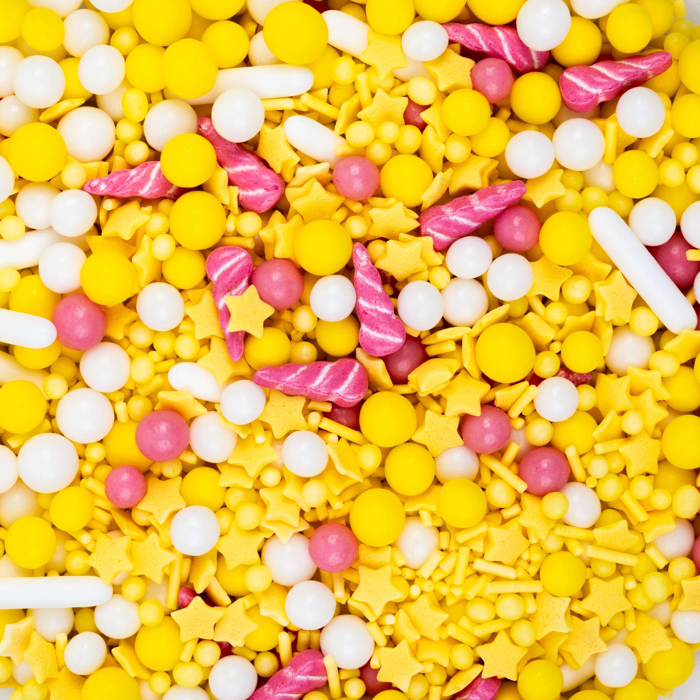 Nahaufnahme des Sallys Streuselwelt Sunshine Mix mit gelben, weißen und rosafarbenen Zuckerstreuseln, Sternen, Perlen und pinken Einhorn-Hörnchen.