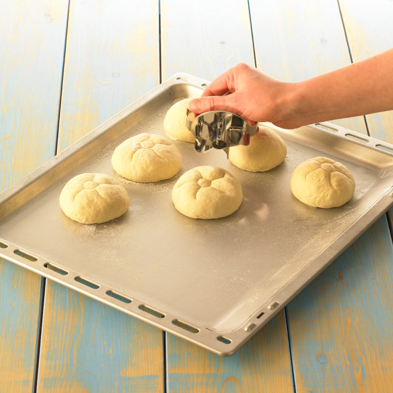 Hand stempelt Brötchenteiglinge auf einem Backblech mit einem klassischen Brötchenstempel ein.