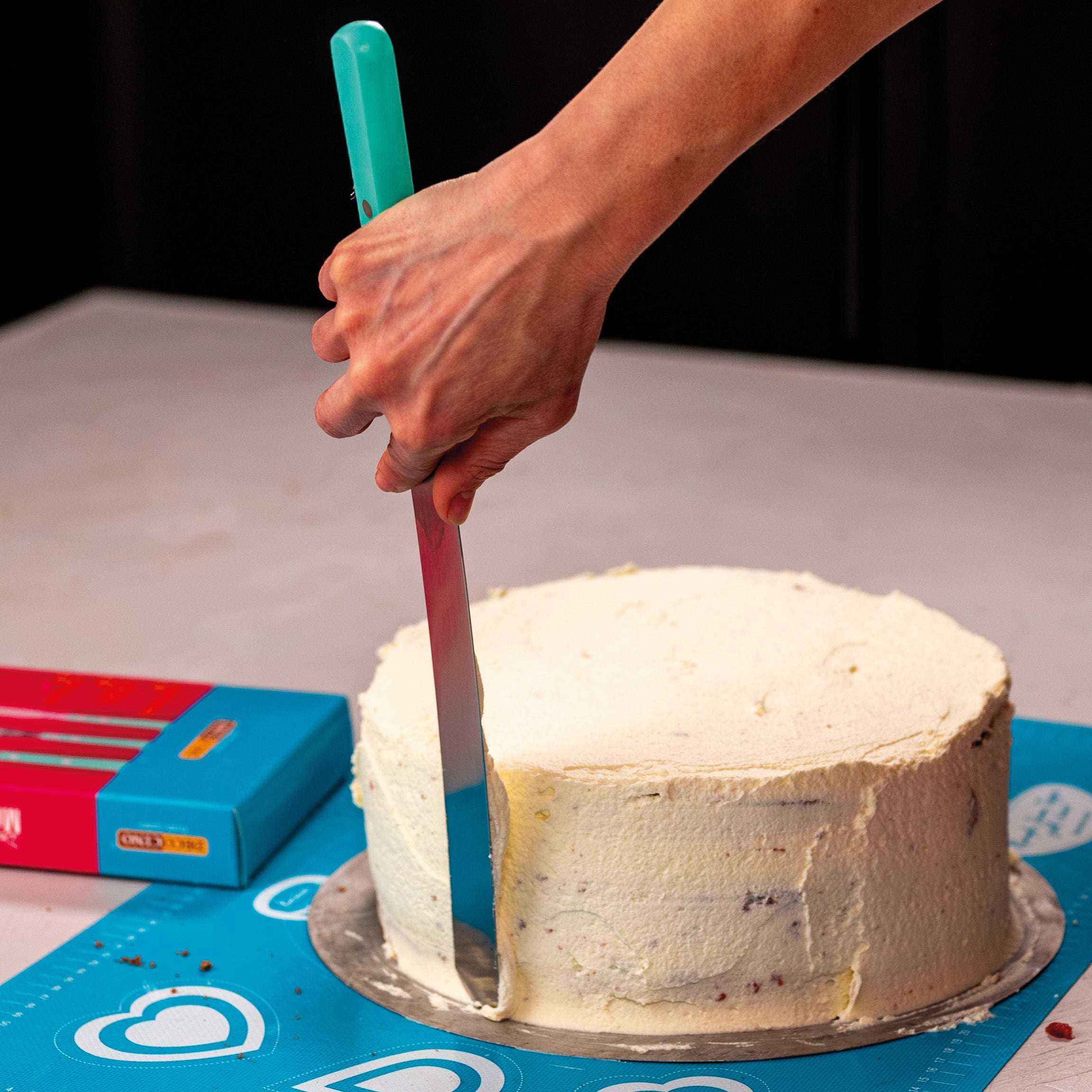 Hand glättet eine Torte mit der langen Decocino Streichpalette mit mintfarbenem Griff.