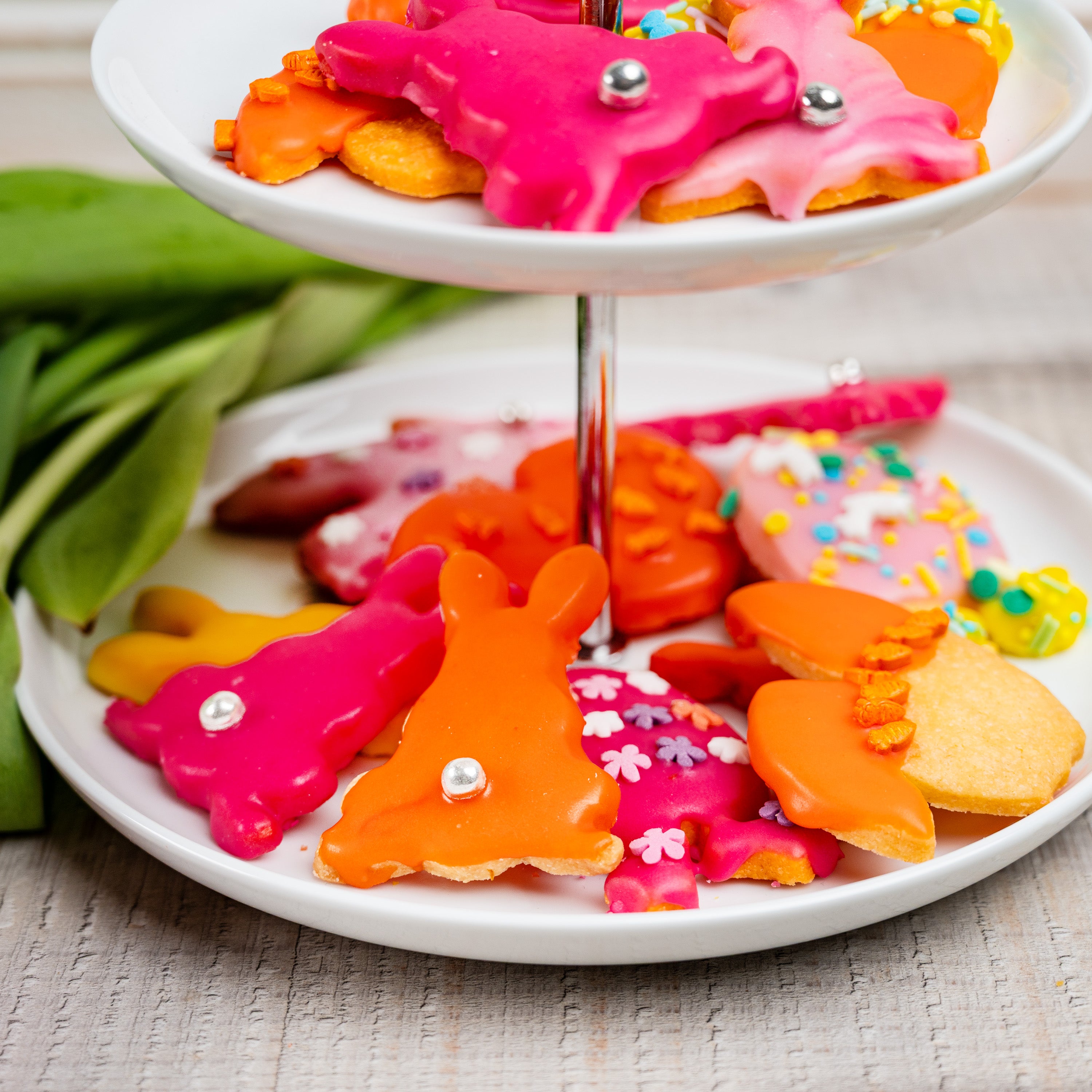 Bunte Osterkekse in Hasen- und Frühlingsformen auf einer weißen Etagere, dekoriert mit farbigem Zuckerguss