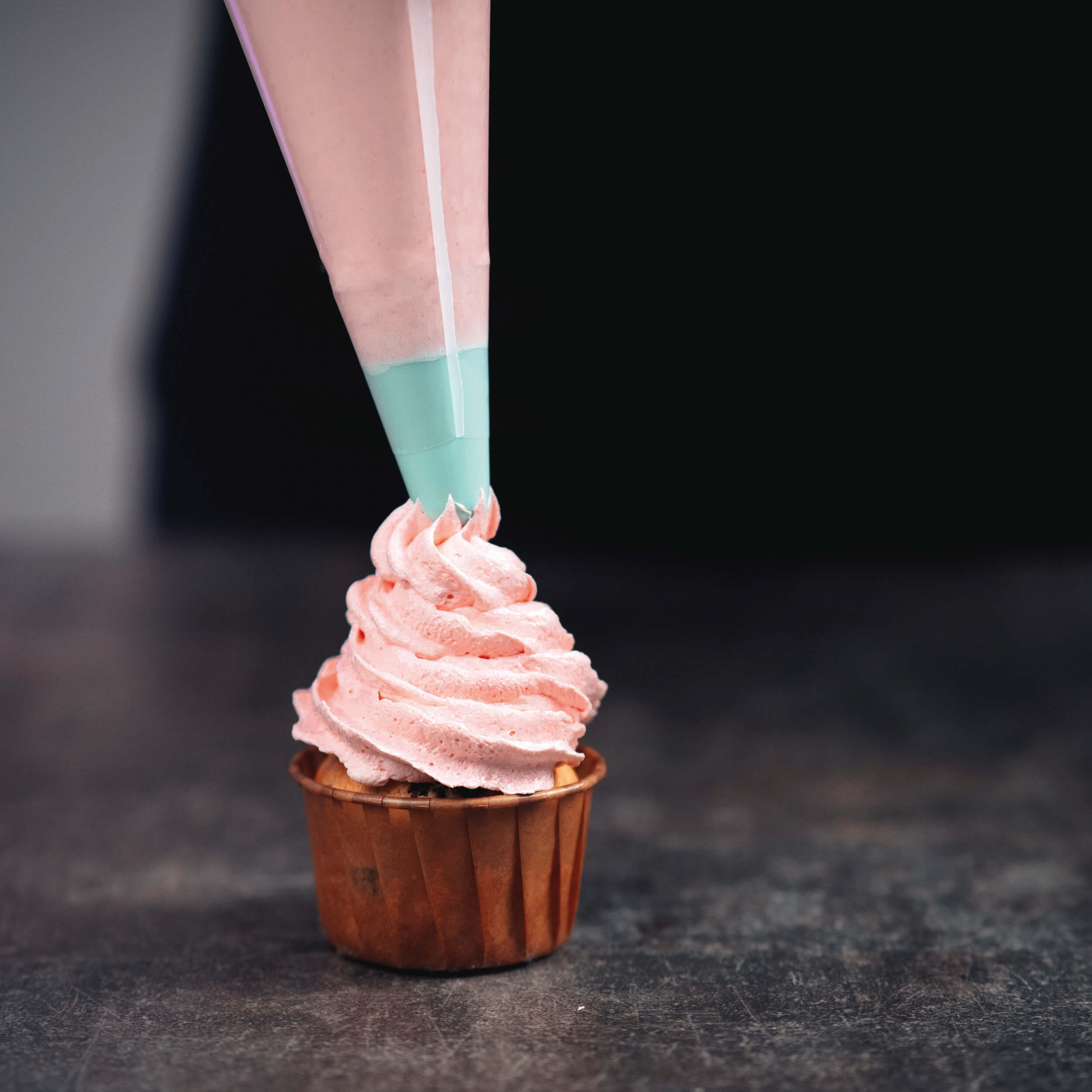 Cupcake wird mit rosa Creme aus einem Spritzbeutel dekoriert