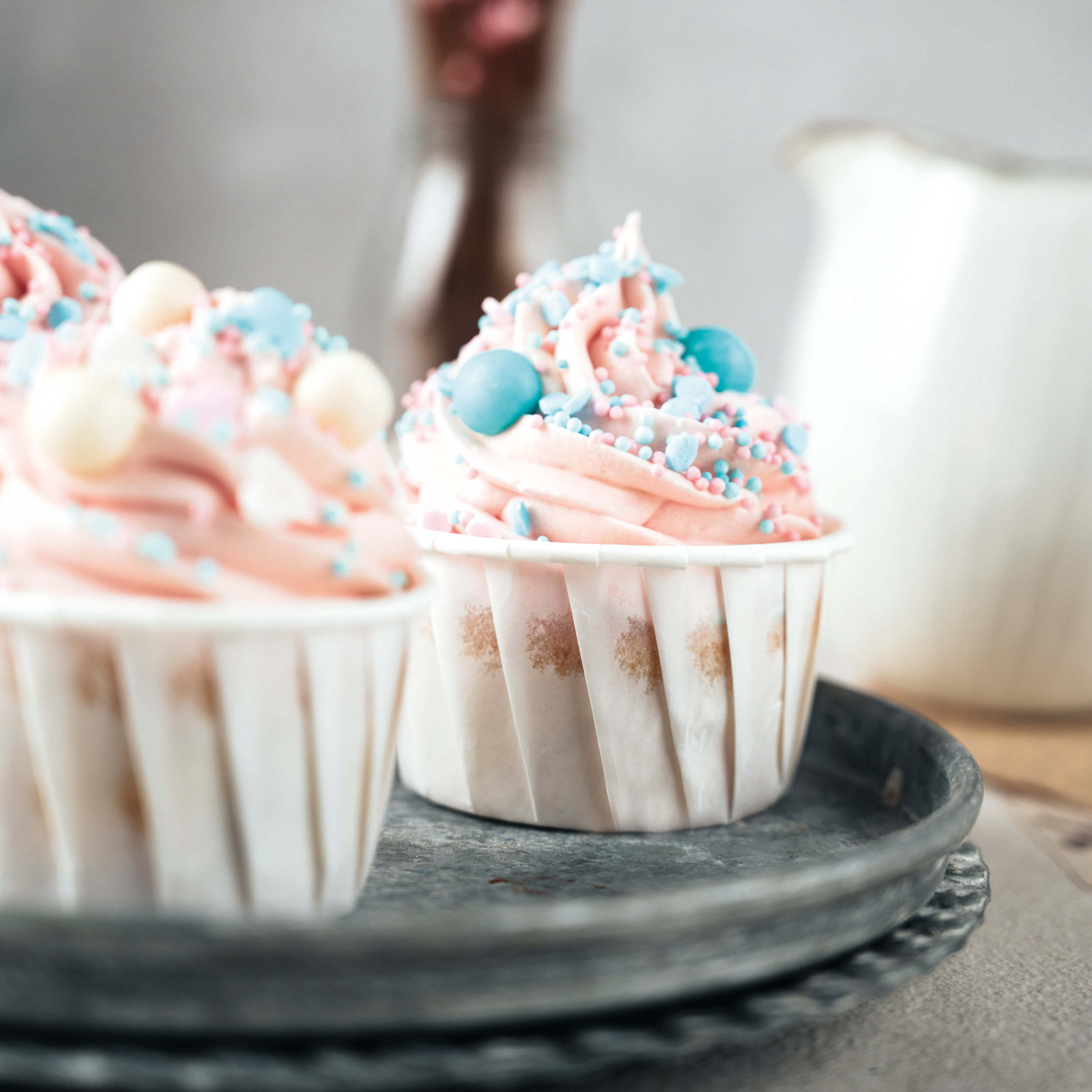Cupcakes mit rosa Creme und pastellfarbenen Decocino Streuseln auf einem Servierteller