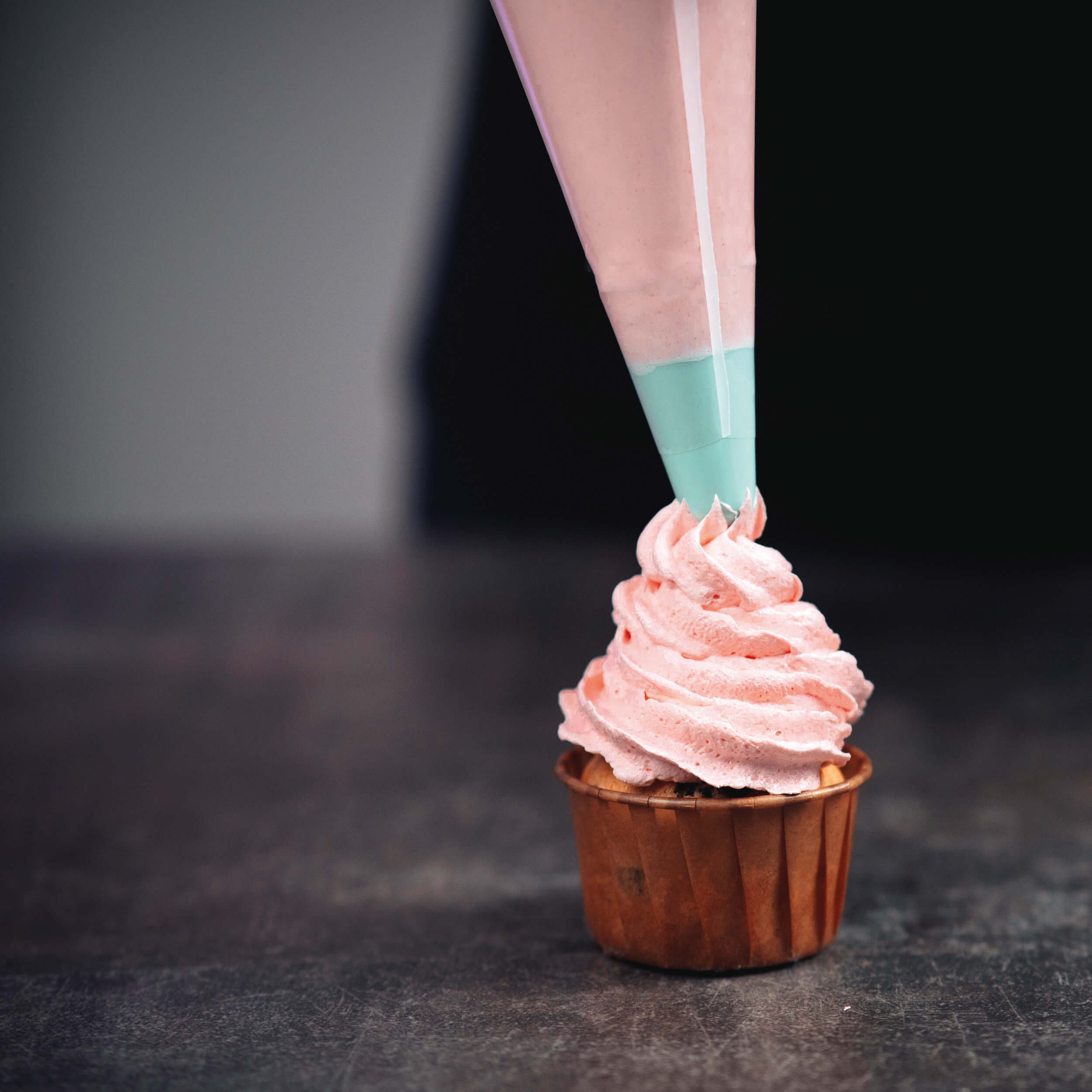 Cupcake wird mit rosa Creme aus einem Spritzbeutel dekoriert