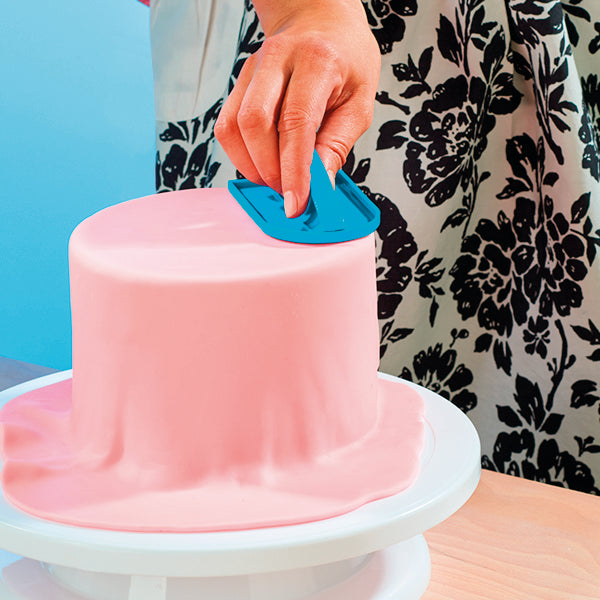 Hand glättet rosa Fondant auf einer Torte mit einem blauen Fondant-Smoother.