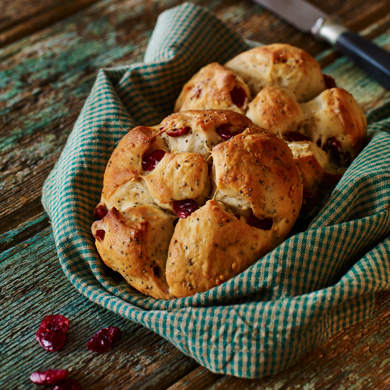 Frisch gebackenes Brötchen mit Cranberries, serviert in einem Küchentuch auf rustikalem Holztisch.
