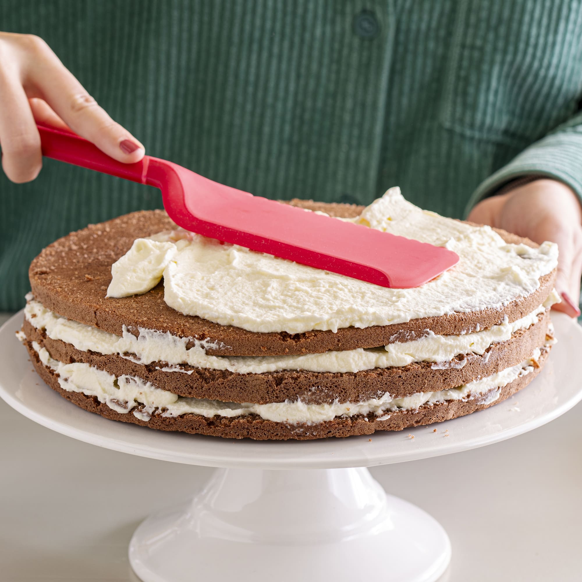 Roter Schneidheber verstreicht Sahnecreme auf einer mehrschichtigen Torte