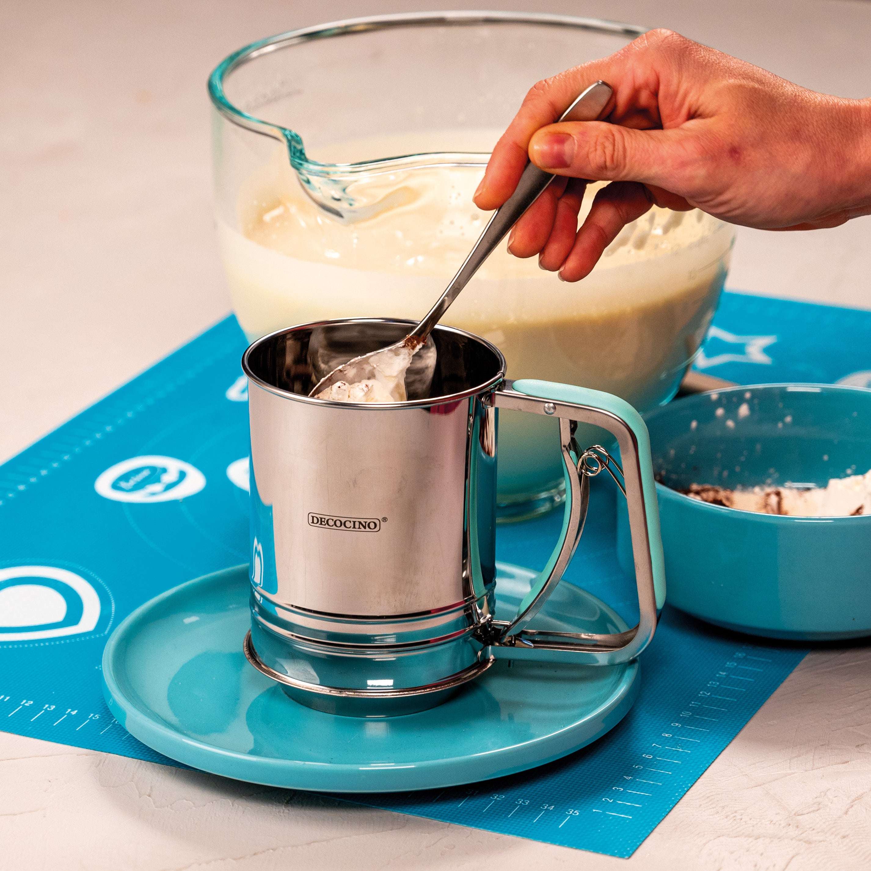 Hand füllt Mehl in das Decocino Einhand-Mehlsieb aus Edelstahl beim Backen in der Küche.
