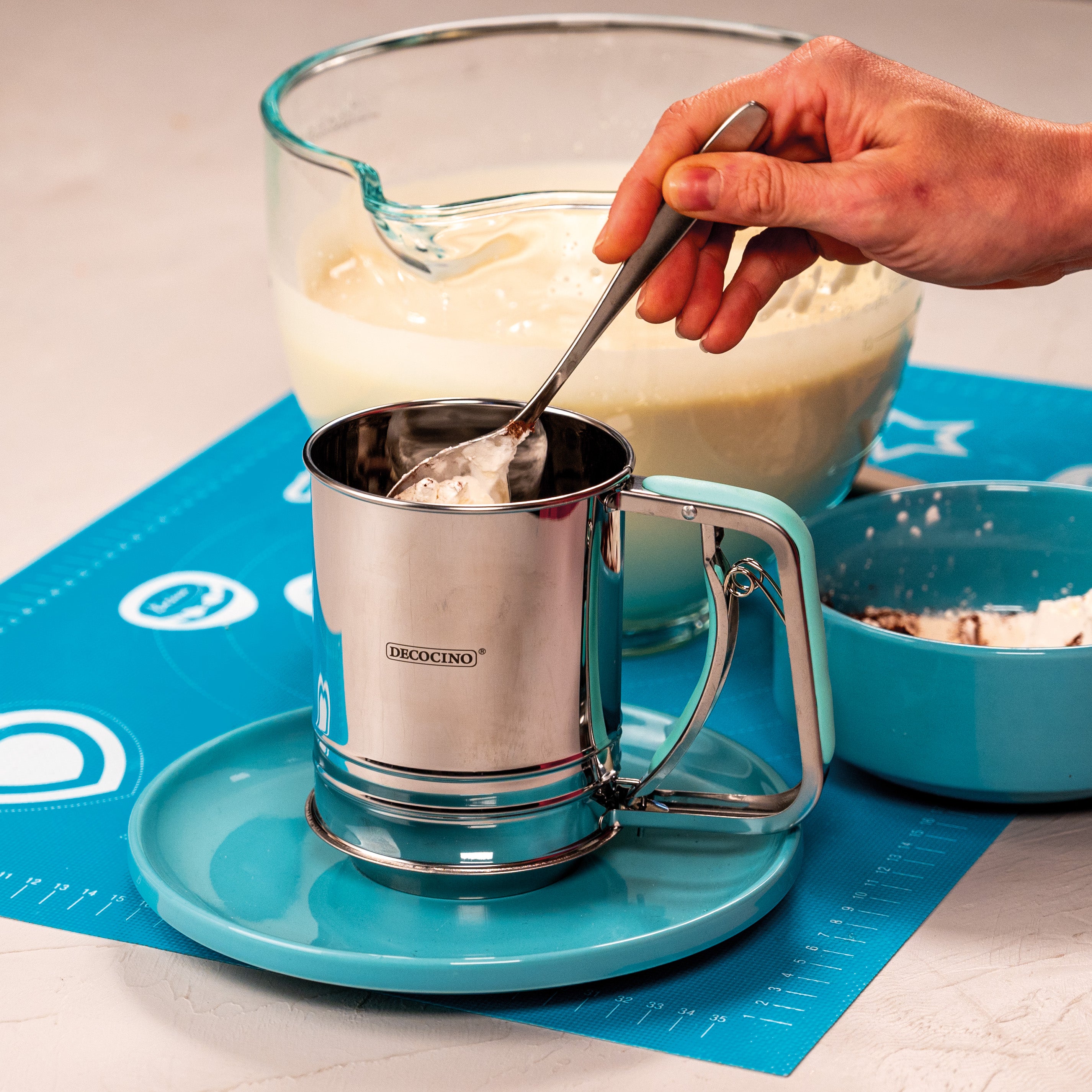 Hand füllt Mehl in das Decocino Einhand-Mehlsieb aus Edelstahl beim Backen in der Küche.
