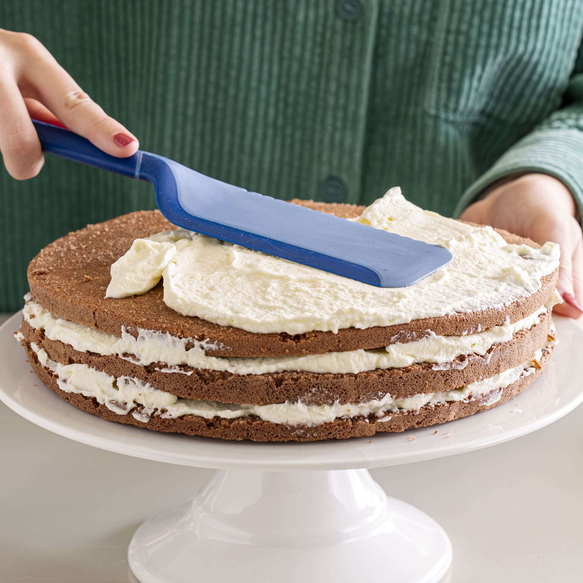 Blauer Schneidheber verstreicht Sahnecreme auf einer mehrschichtigen Torte.
