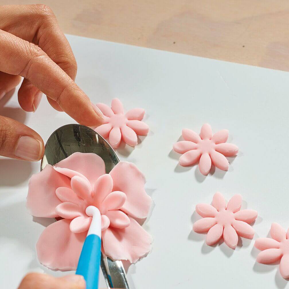 Hand formt mit Modellierwerkzeug eine zarte rosa Fondantblume auf einem Löffel