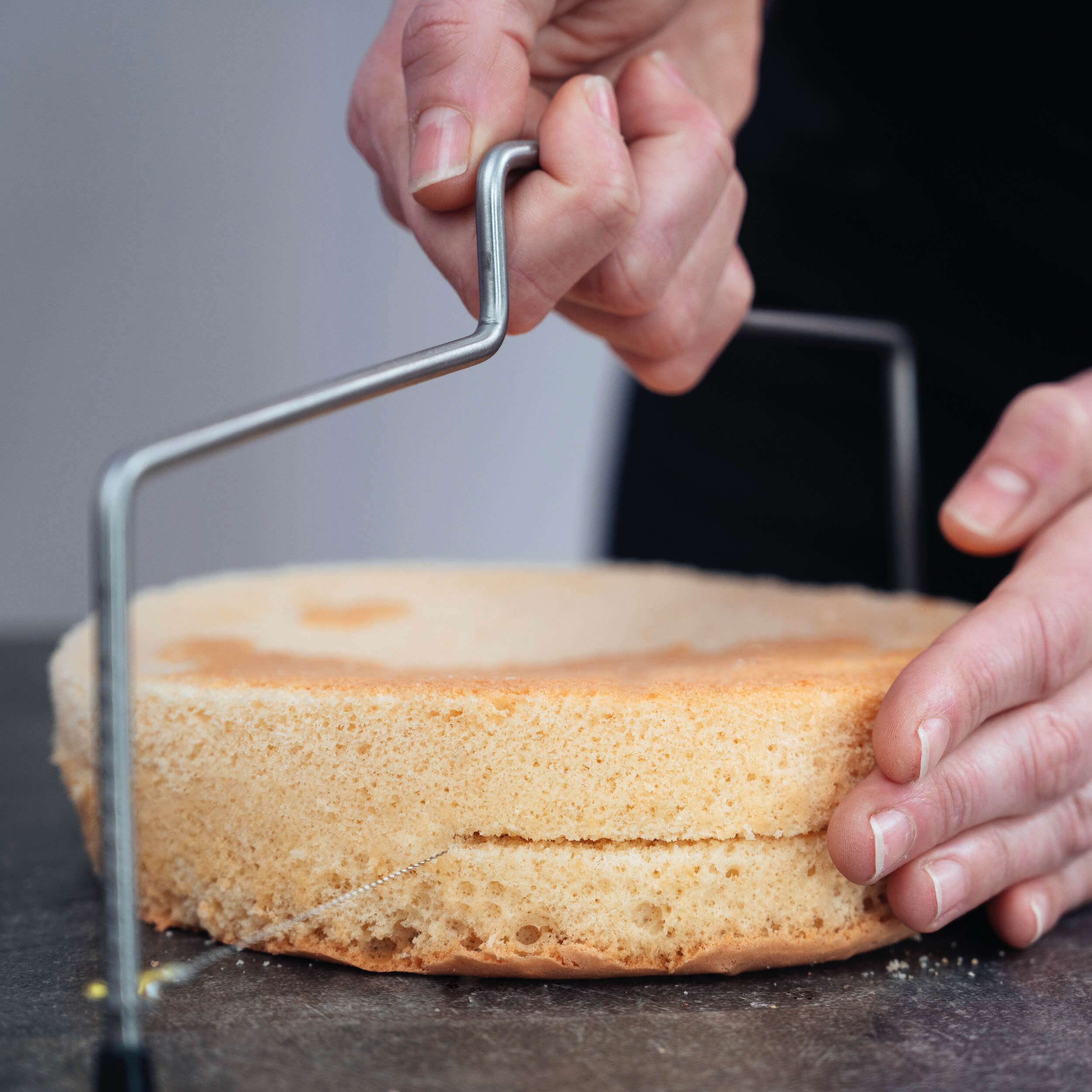 Person schneidet einen Tortenboden mit dem höhenverstellbaren Decocino Tortenschneider sauber durch